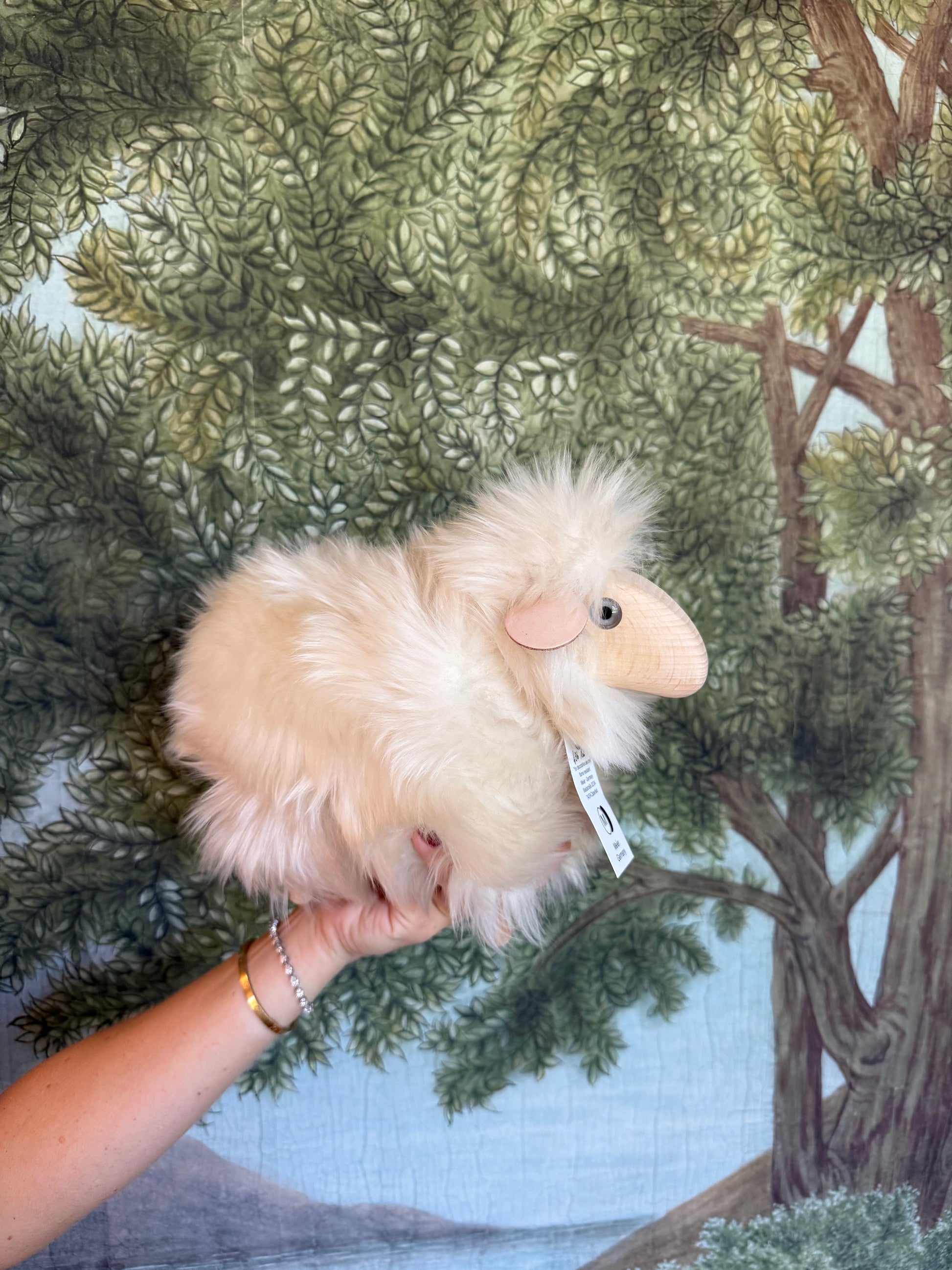 Tiny white Meier lamb held in a hand, showing its size against a forest print backdrop
