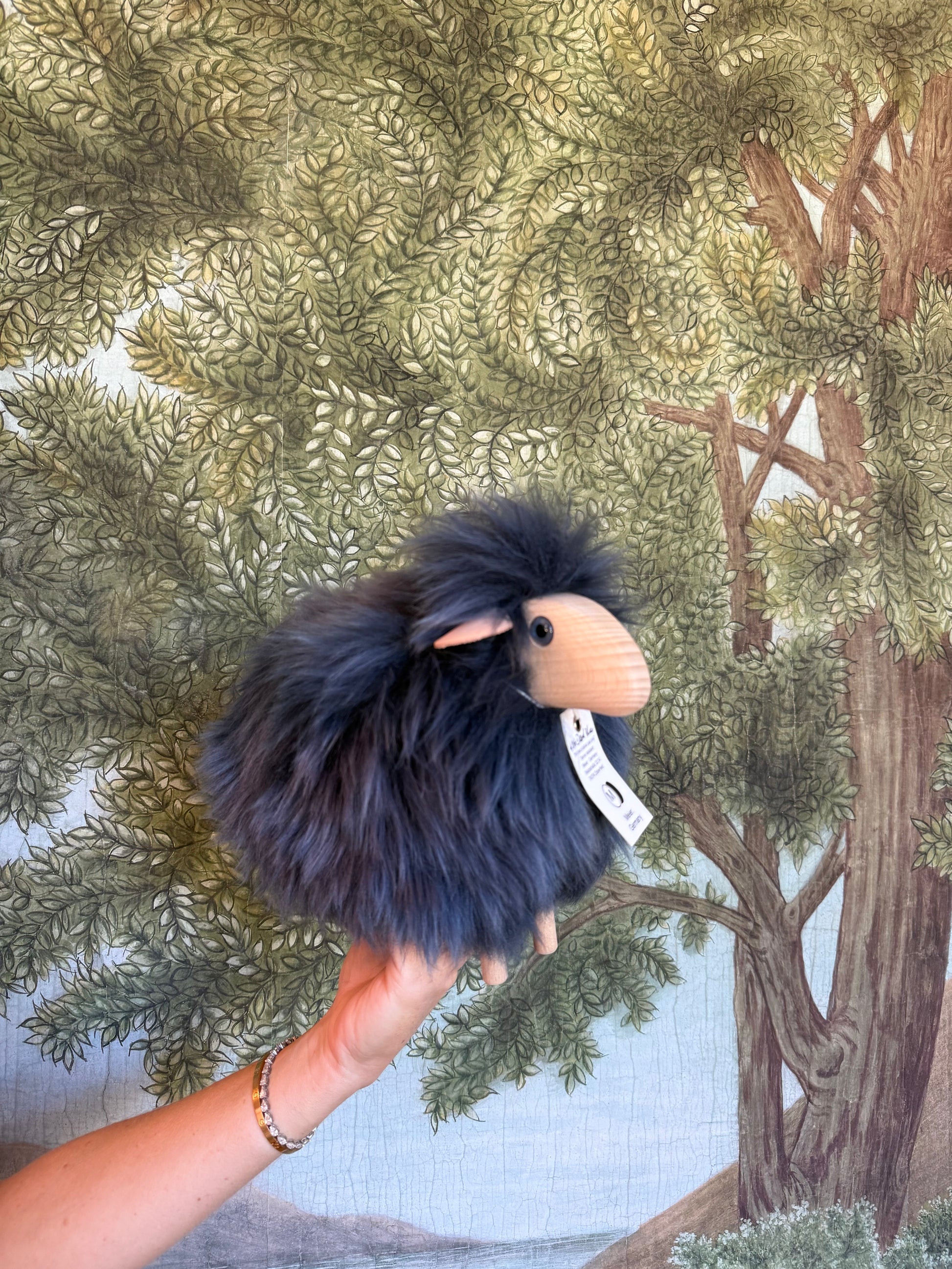 Navy blue tiny lamb resting in a hand, woodland print fabric behind it