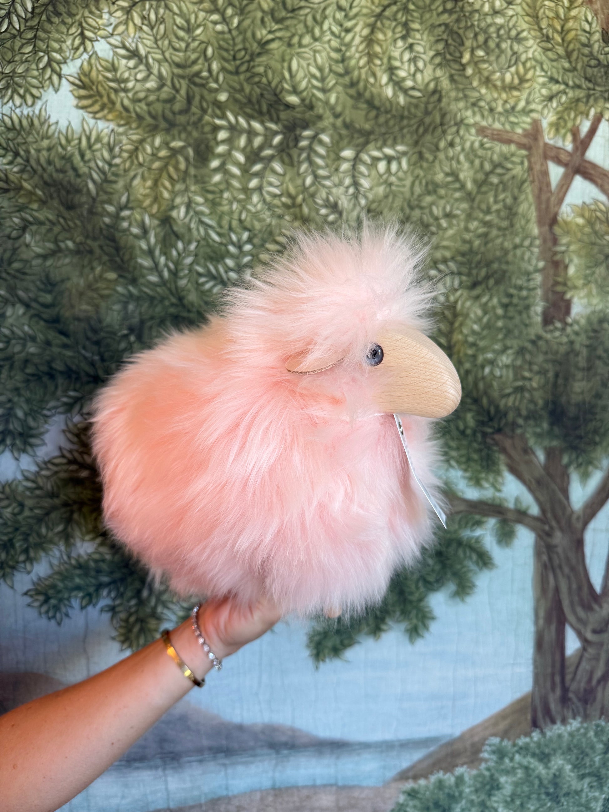 Pale pink tiny lamb held in a hand against a printed woodland scene