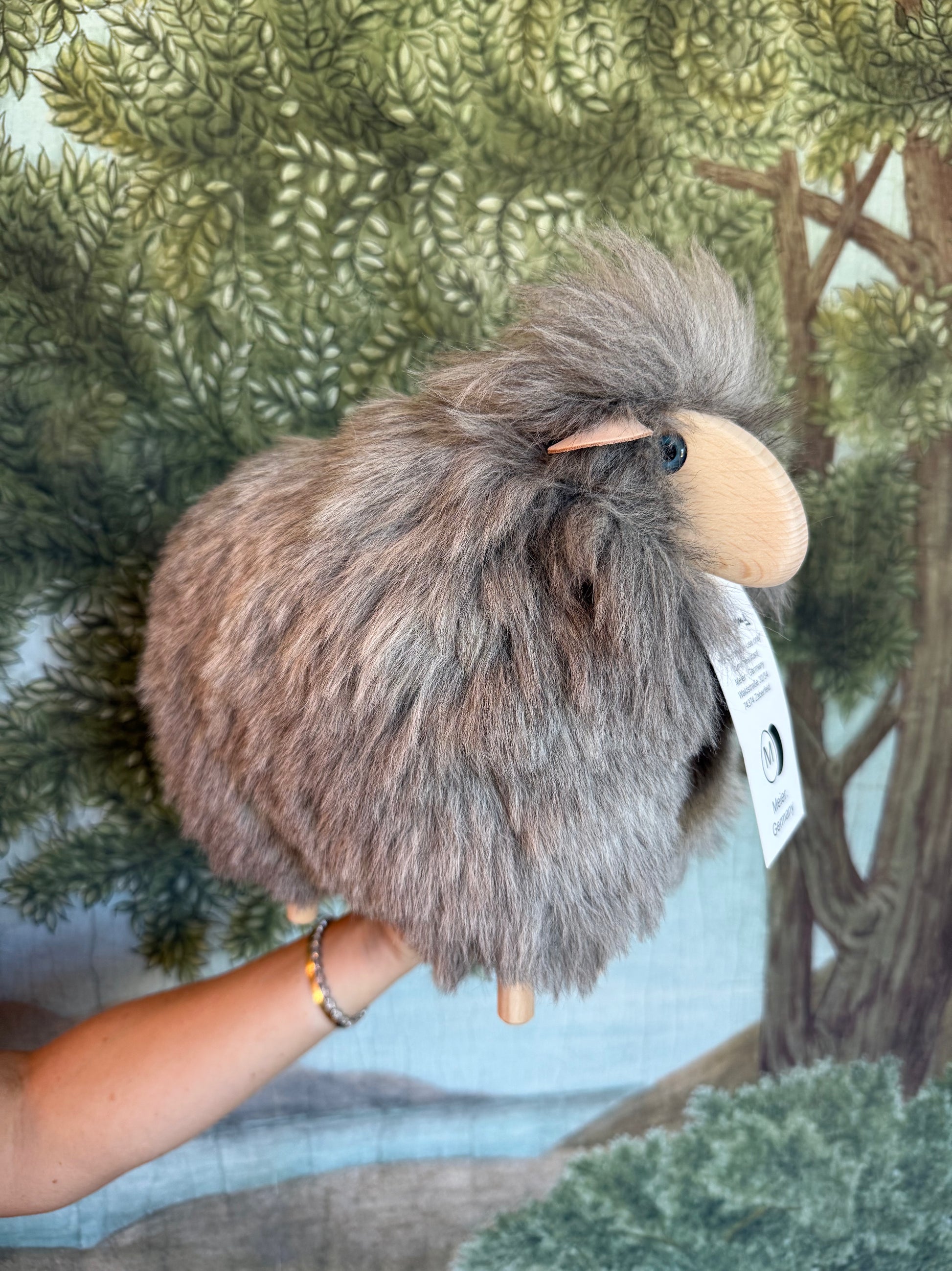 Grey lamb held in a hand, price tag hanging, woodland print behind