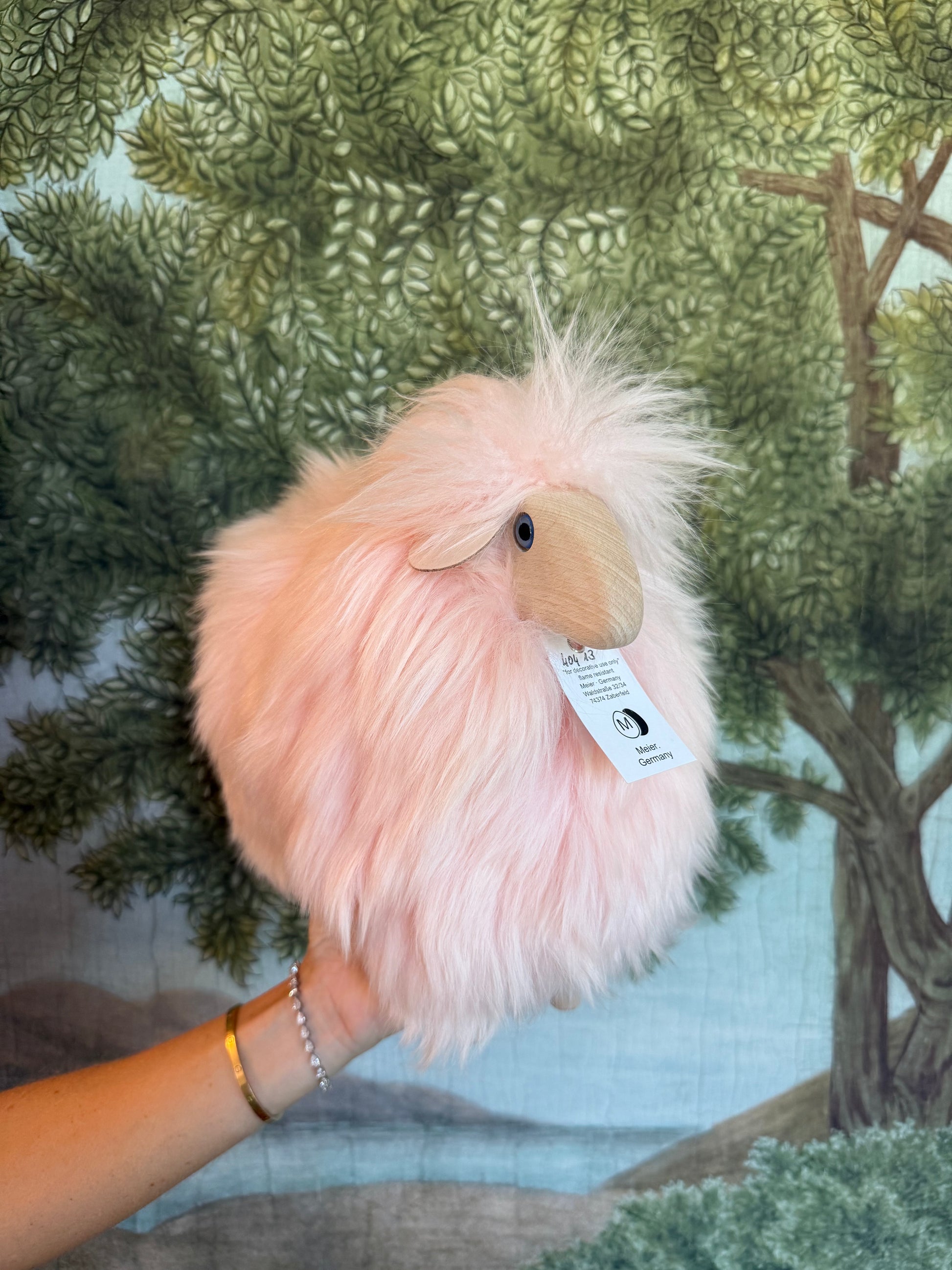 Pink little lamb held in a hand, swing tag showing, forest print behind