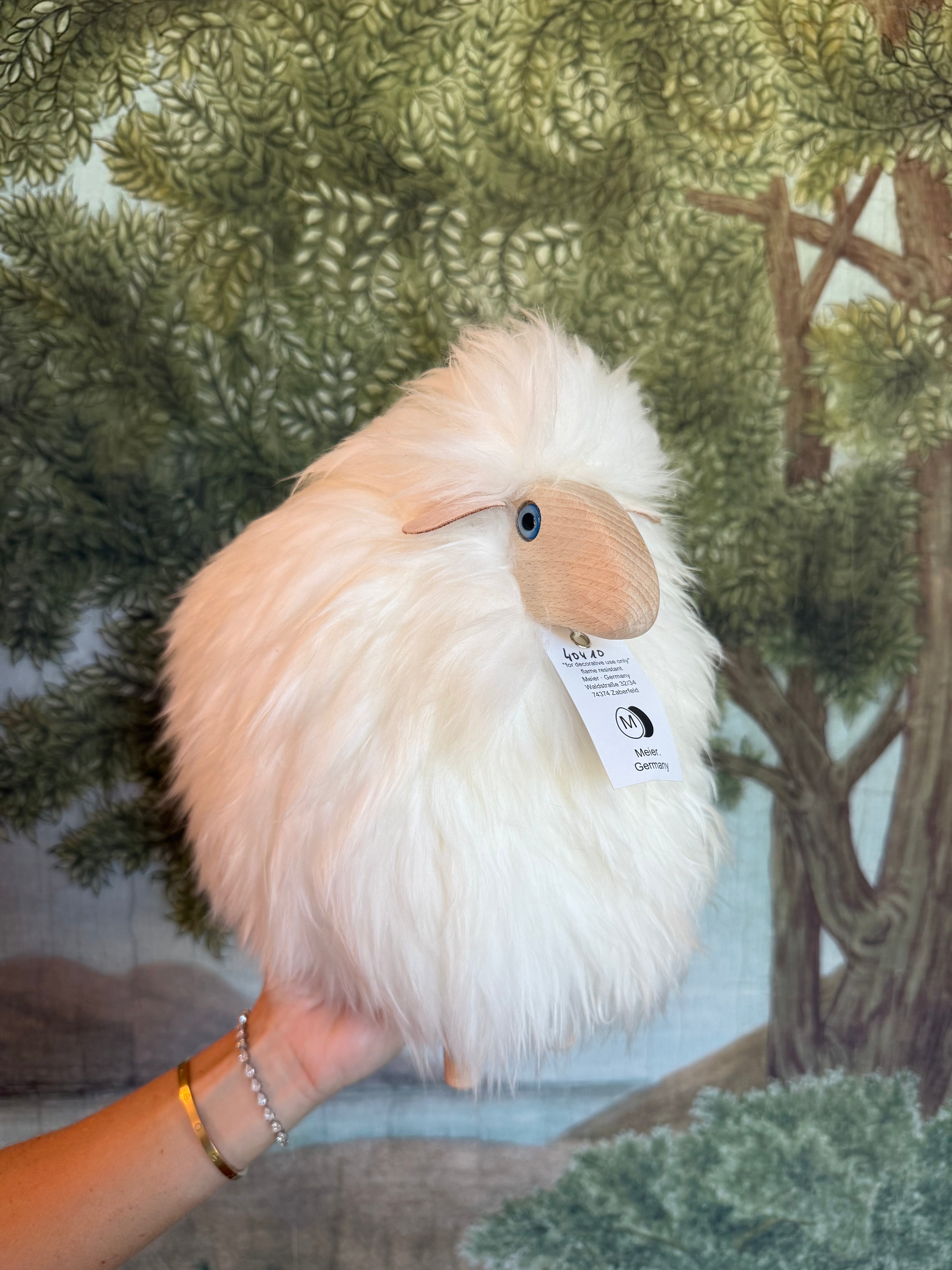 White little lamb held in a hand against a woodland print backdrop